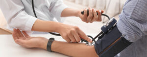 Aerztin misst den Blutdruck am Arm des Patienten mit einem manuellen Blutdruckmessgeraet